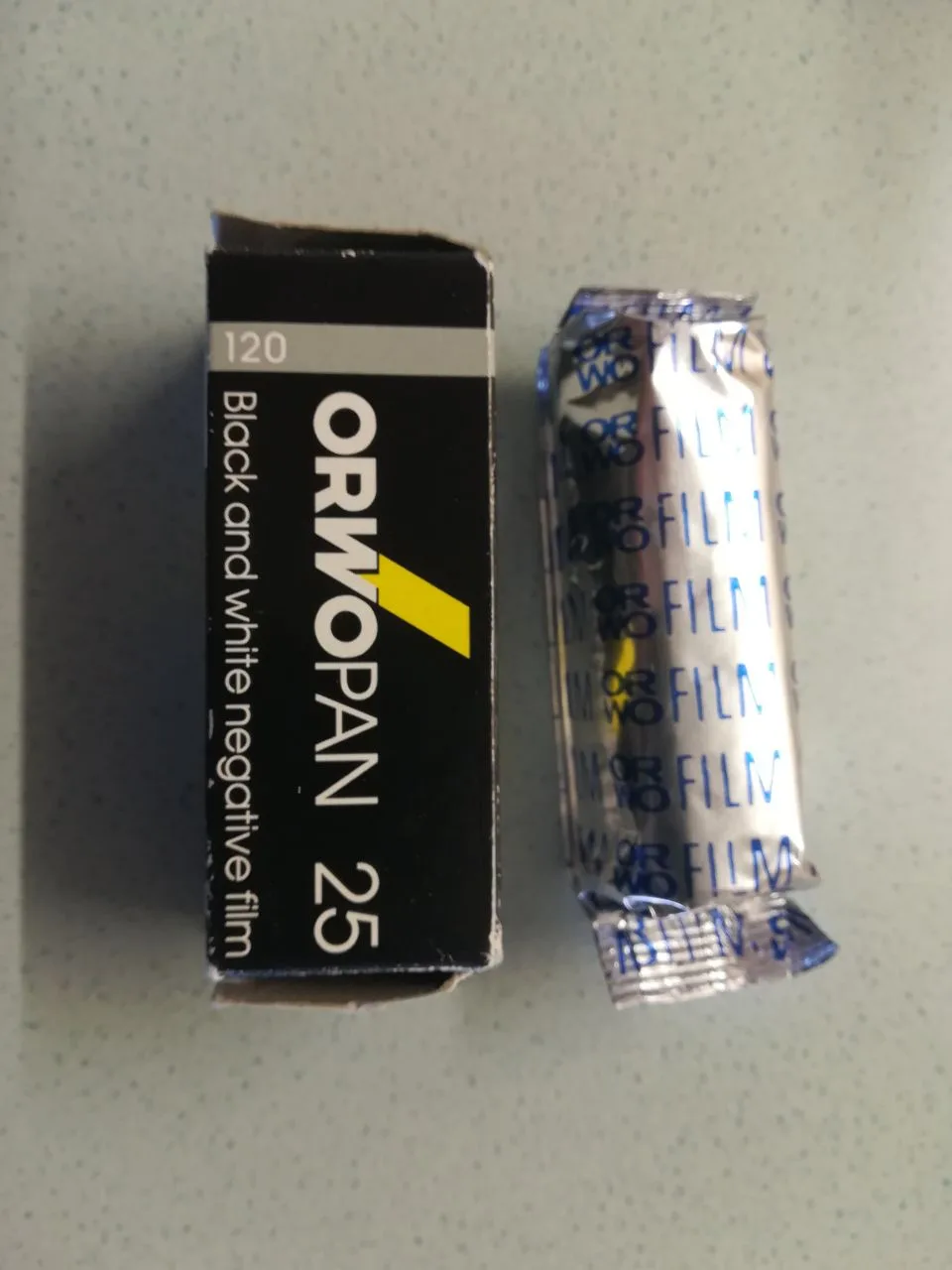 A roll of ORWO PAN 25 120 film beside its box — ORWO is the East German manufacturer FilmoTec was spun out of
